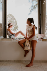 Deux filles devant la fenêtre dans un mas provencal, avec le pochon Chouette et la gamme de produits  responsables et certifies bio pour les enfants