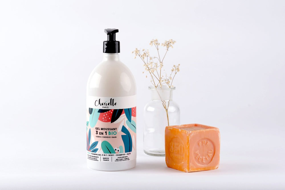 Flacon de gel moussant devant un savon de Marseille orange et  un brin d'immortelle dans un flacon  verre