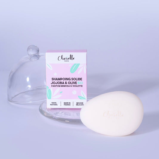 Shampoing solide ovale avec étui à coté d'une cloche en verre